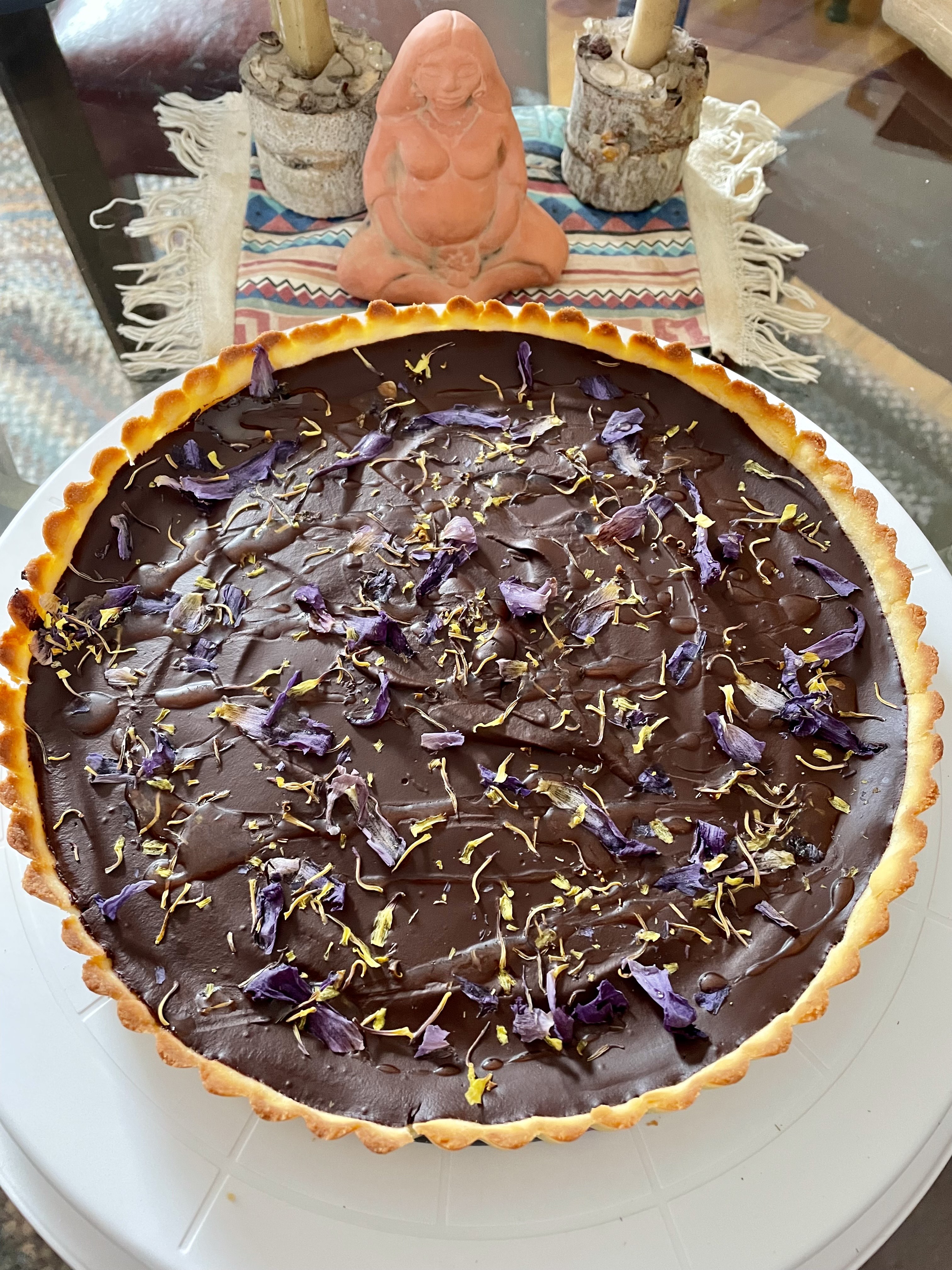 Chocolate tart with flower petals with a goddess altar behind it.
