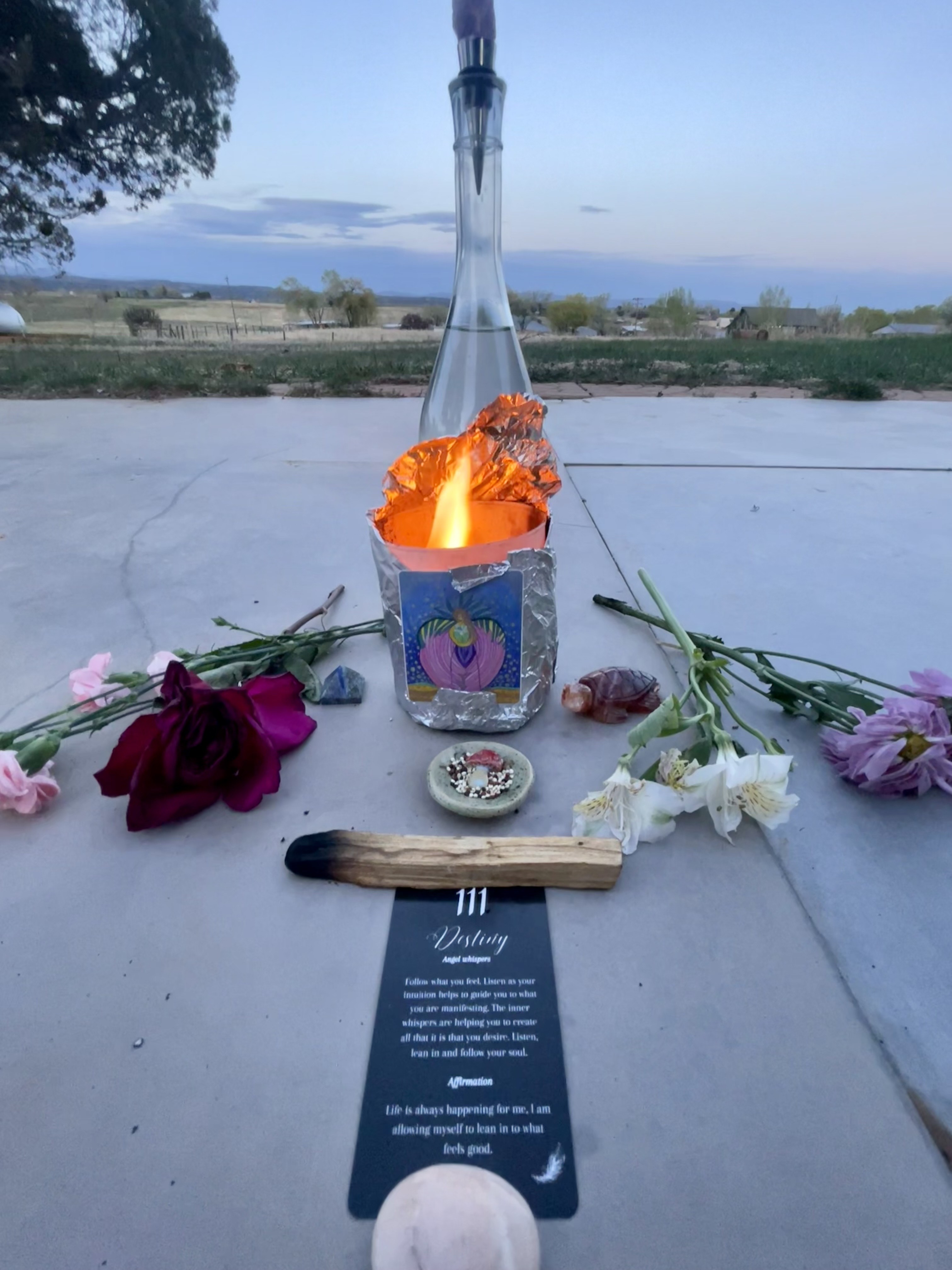 Tall glass bottle with a fire in front of it and flowers surrounding a ceremonial circle.